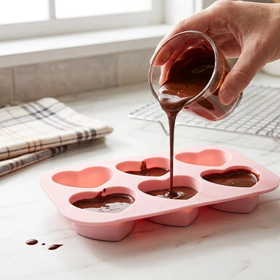 Chocolat fondu versé dans moules en silicone rose en forme de cœur