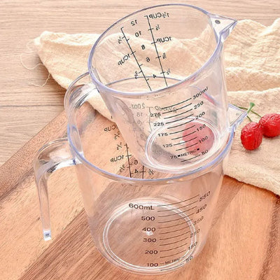 Deux verres doseurs gradués transparents de 300 ml et 600 ml empilés sur plan de travail en bois