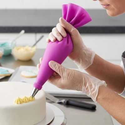 Personne décorant un gâteau avec une poche à douille réutilisable rose pour appliquer uniformément crème et glaçage