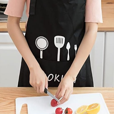 Personne portant un tablier de cuisine noir avec grande poche frontale, découpant des légumes sur une planche à découper