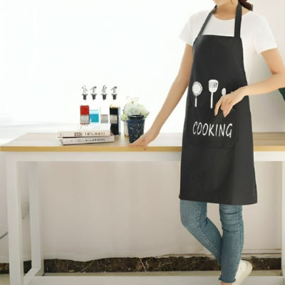 Personne portant un tablier de cuisine noir avec grande poche frontale posant une main sur une table