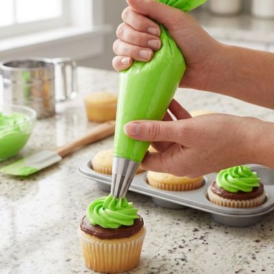 Poche à douille verte décorant un cupcake avec glaçage en spirale dans une cuisine de pâtisserie maison