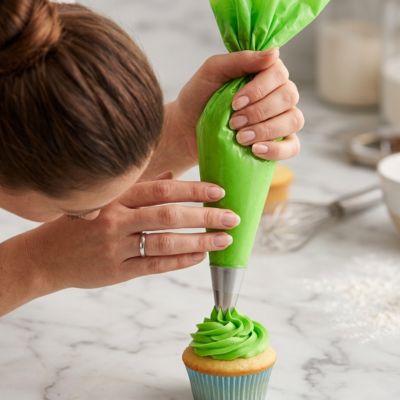 Poche à douille verte utilisée avec précision pour décorer un cupcake avec glaçage dans une cuisine de pâtisserie