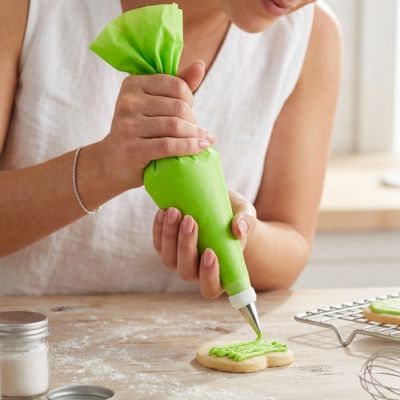 Poche à douille verte utilisée pour décorer un biscuit avec glaçage dans une cuisine de pâtisserie