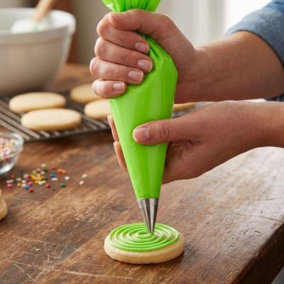 Poche à douille verte utilisée pour décorer un biscuit sablé avec glaçage dans un atelier de pâtisserie maison