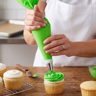 Poche à douille verte utilisée pour décorer un cupcake avec glaçage dans un atelier de pâtisserie maison