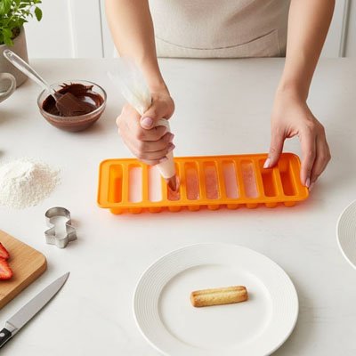 Préparation de bâtonnets glacés maison avec moule silicone orange et poche à douille en cuisine