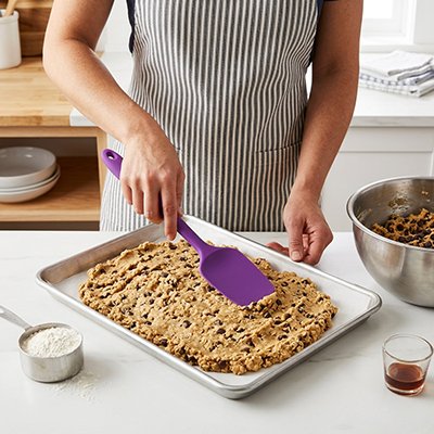 Spatule Cuisine en silicone violette utilisée pour étaler une pâte à biscuits sur une plaque de cuisson