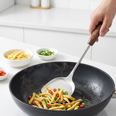 Spatule cuisine en acier inoxydable avec manche en bois utilisée pour faire sauter légumes dans wok