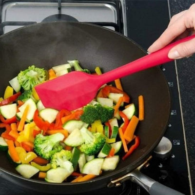 Spatule de cuisine en silicone rouge utilisée pour faire sauter des légumes dans une poêle antiadhésive
