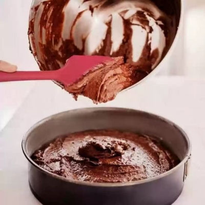 Spatule en silicone rouge utilisée pour verser une pâte au chocolat dans un moule à gâteau