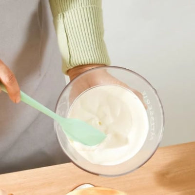 Spatule en silicone verte mélangeant une crème dans un bol transparent