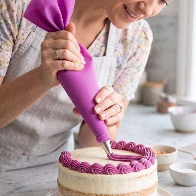 Utilisation d une poche à douille pâtisserie réutilisable rose pour créer une bordure décorative précise avec crème colorée sur un gâteau