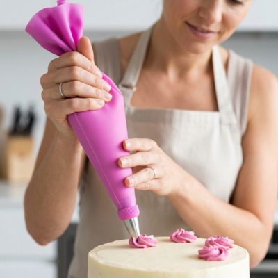 Utilisation d’une poche à douille pâtisserie rose pour appliquer une crème décorative régulière sur un gâteau fait maison