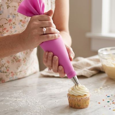 Utilisation dune poche à douille réutilisable rose pour appliquer une décoration crémeuse et régulière sur un cupcake