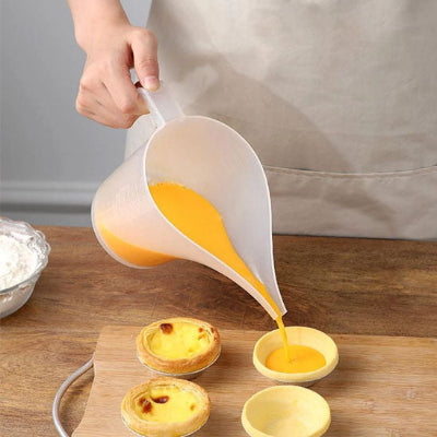 Verre doseur au long bec verseur remplissant des moules à tartelettes avec une préparation aux œufs