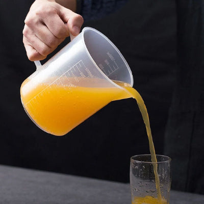 Verre doseur gradué transparent avec poignée ergonomique versant du jus dans un verre