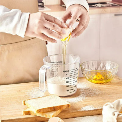 Verre doseur gradué transparent utilisé pour mélanger de farine et œuf lors de préparation recette de pâtisserie