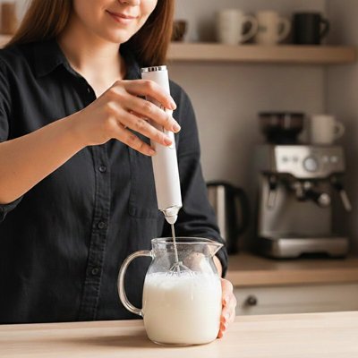 Femme plongent mousseur à lait dans un verre sur une table 