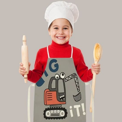 petit garçon portant tablier de cuisine enfant motif pelleteuse tenant rouleau pâtisserie et cuillère en bois