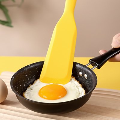 spatule en silicone jaune retournant œuf au plat dans poêle antiadhésive